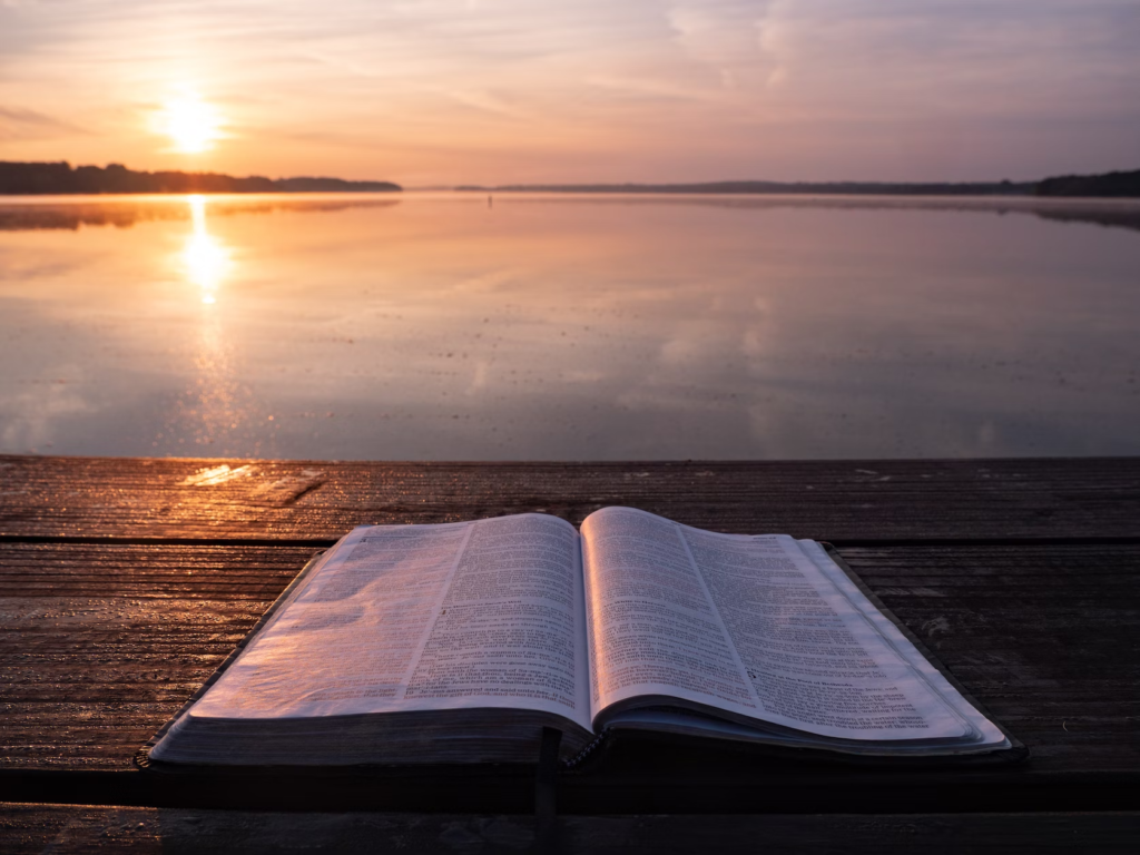 A Bible placed on a pier as someone reads it during a beautiful sunset. 
